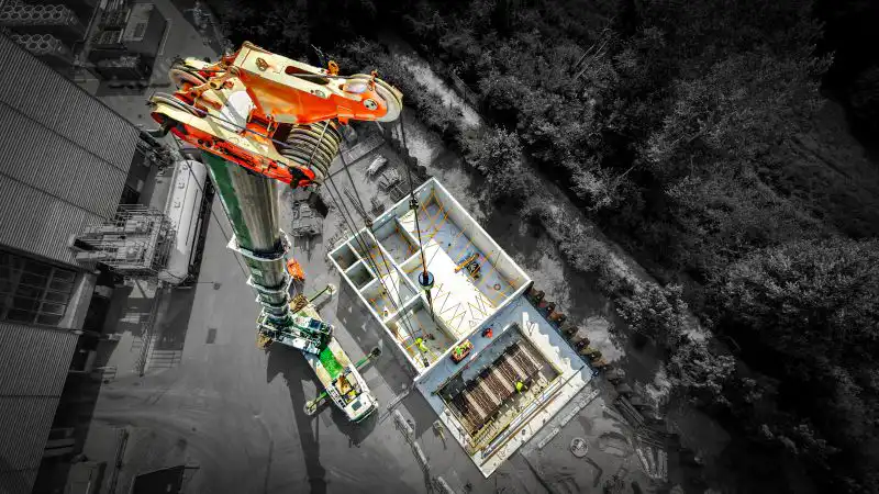 Dronebillede fra toppen af en kran, imens den løfter byggeelementer til hus